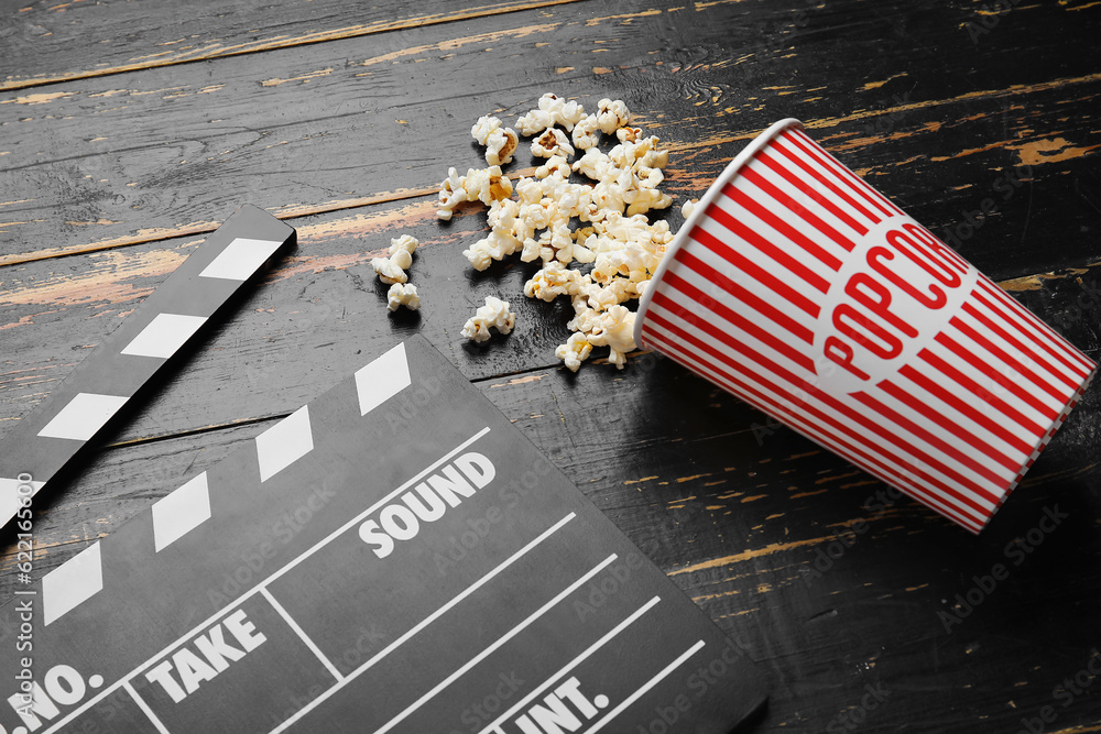 Bucket with tasty popcorn and clapperboard on black wooden background