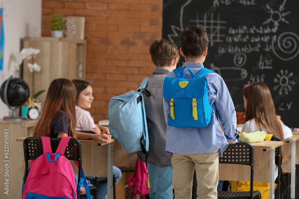 Little pupils with backpacks in classroom, back view