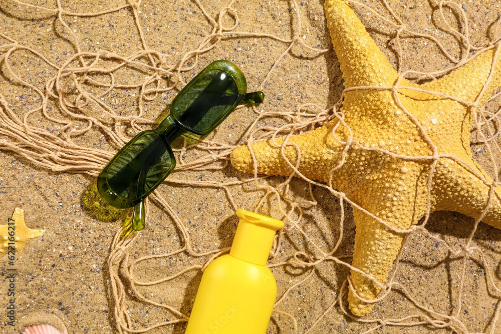 Sunglasses with starfishes and bottle of sunscreen cream on sand