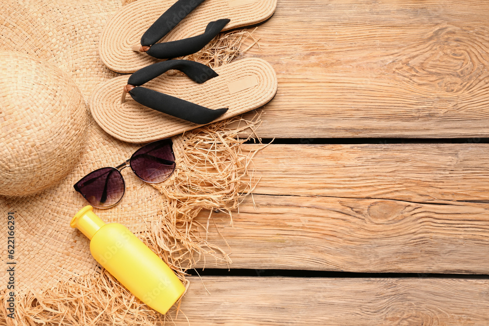 Sunglasses with flip flops, wicker hat and bottle of sunscreen cream on wooden background