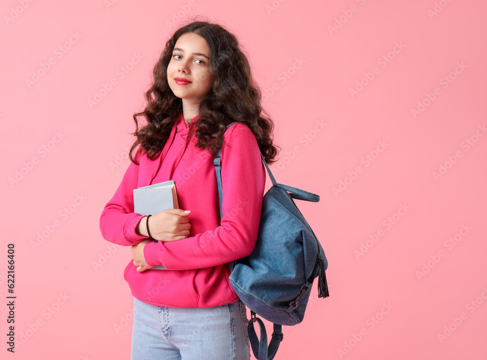 Female student with book and backpack on pink background