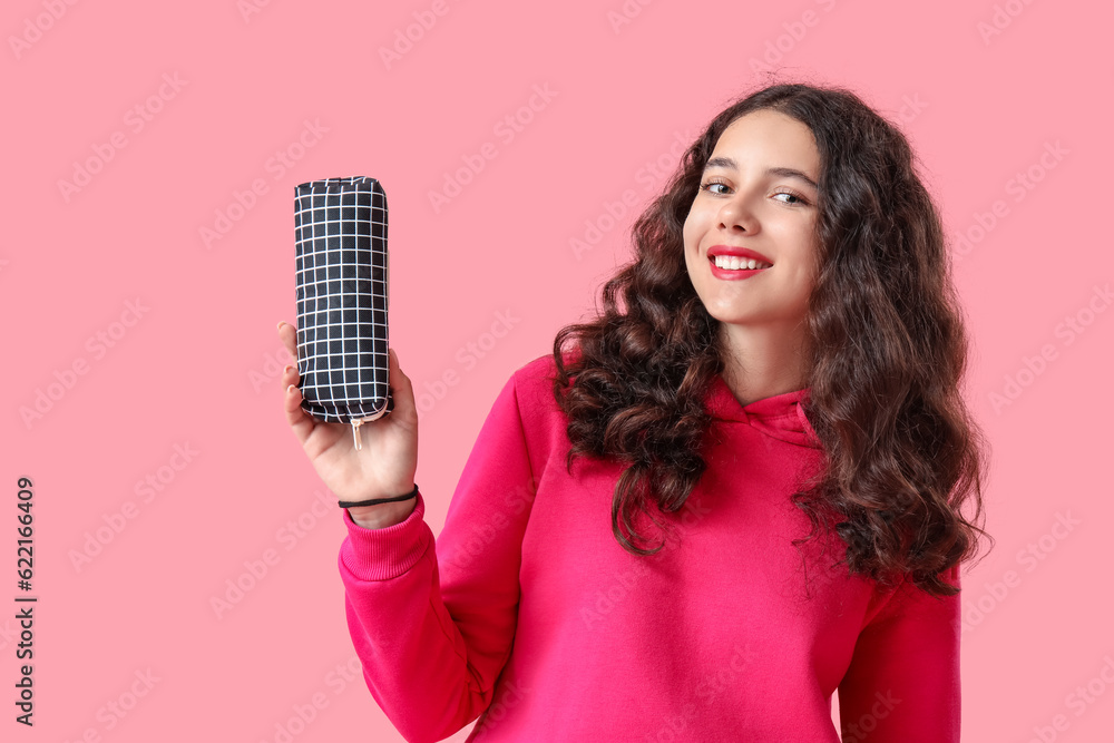 Female student with pencil case on pink background