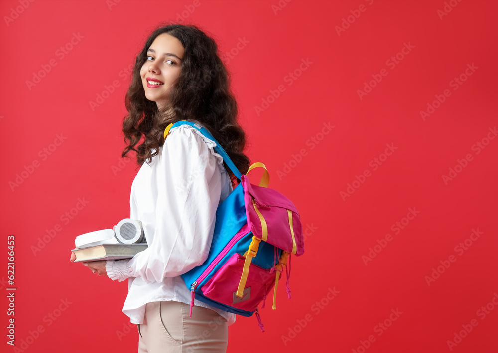 Female student with headphones, book and backpack on red background