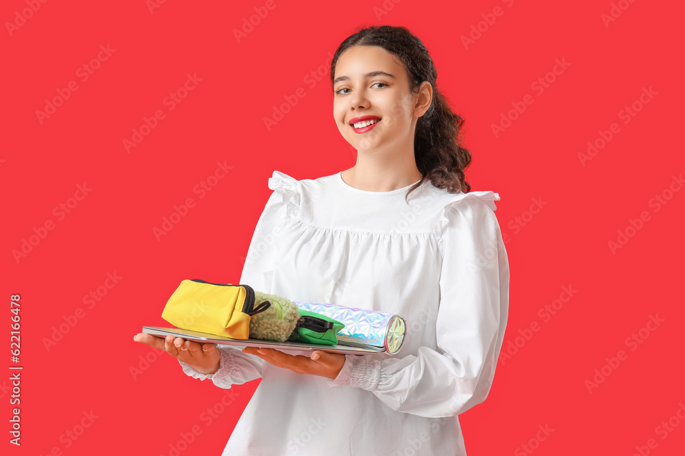 Female student with pencil cases and laptop on red background