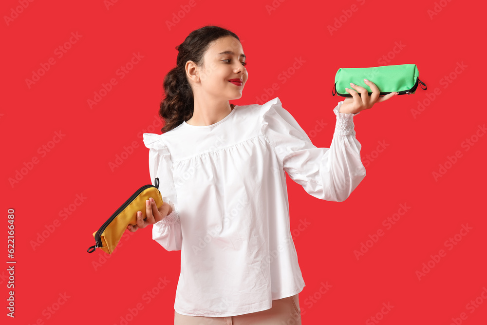 Female student with pencil cases on red background