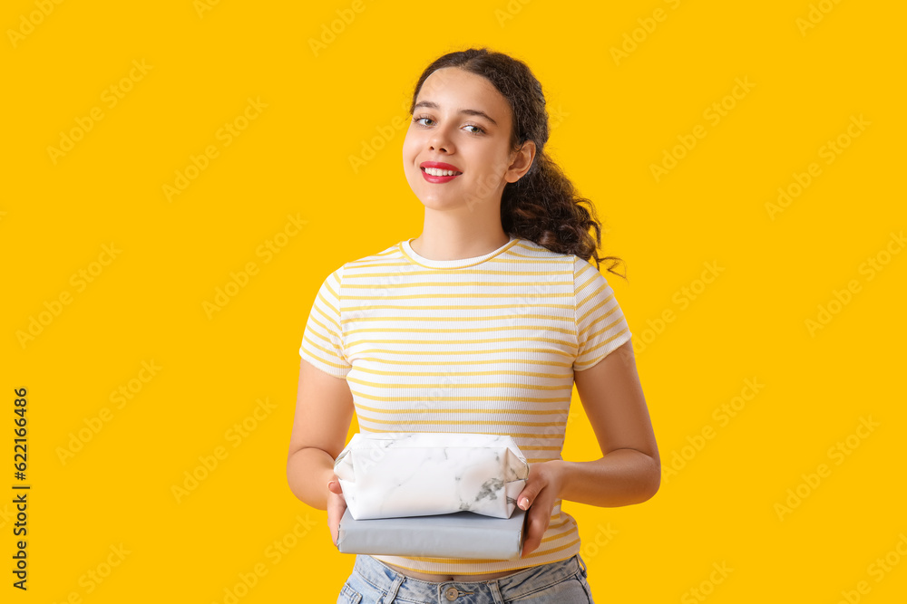 Female student with pencil case and book on yellow background