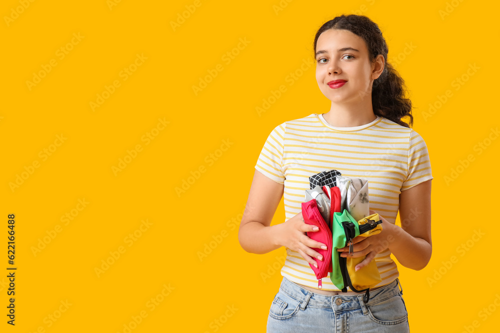 Female student with pencil cases on yellow background