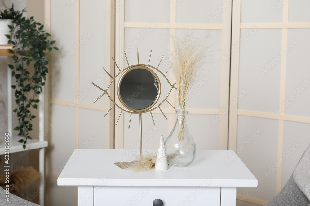 Mirror and vase with dried plant on table in living room, closeup