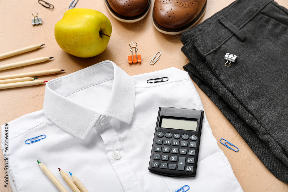 Different stationery with stylish school uniform and fresh apple on beige background