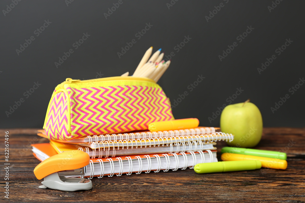 Different stationery with fresh apple on wooden table against black chalkboard