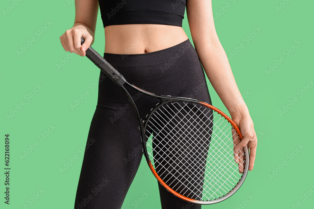 Young woman in sportswear and with tennis racket on green background