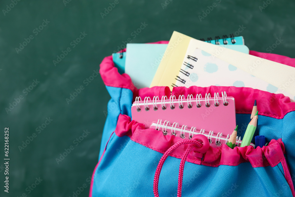 Colorful school backpack with notebooks and pencils on green background