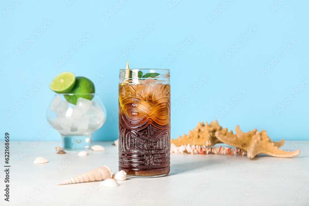 Glass of cold Cuba Libre cocktail, seashells and starfishes on white table