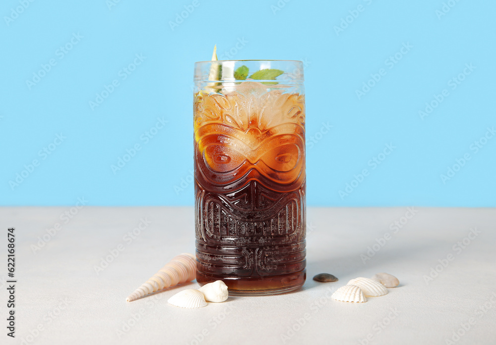 Glass of cold Cuba Libre cocktail and seashells on white table