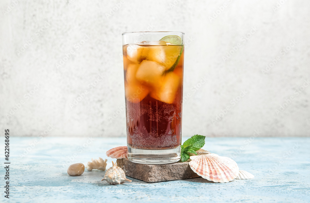 Stone with glass of cold Cuba Libre cocktail and seashells on blue table