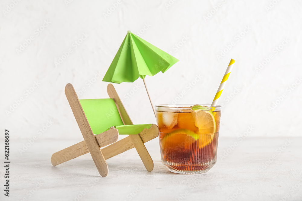 Glass of cold Cuba Libre cocktail and deckchair on white background