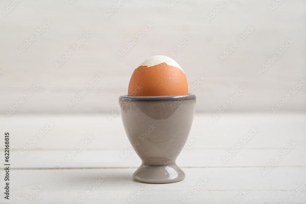 Holder with boiled chicken egg on white wooden background