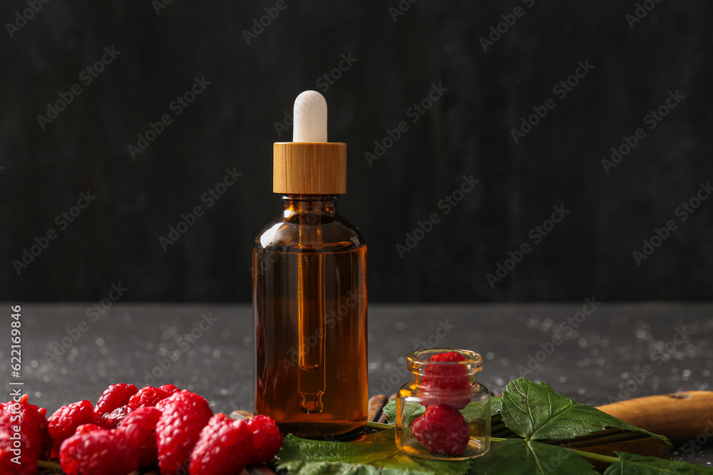 Wooden board with bottle of cosmetic raspberry oil on black background