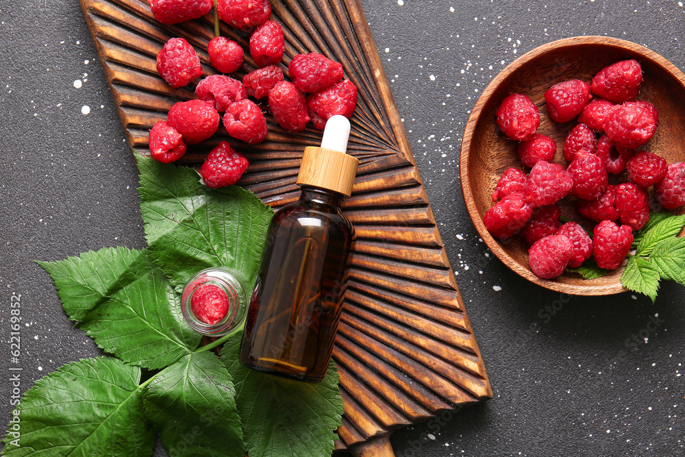 Wooden board with bottle of cosmetic raspberry oil on black background