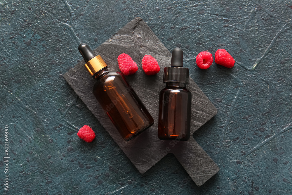 Board with bottles of cosmetic raspberry oil on dark background