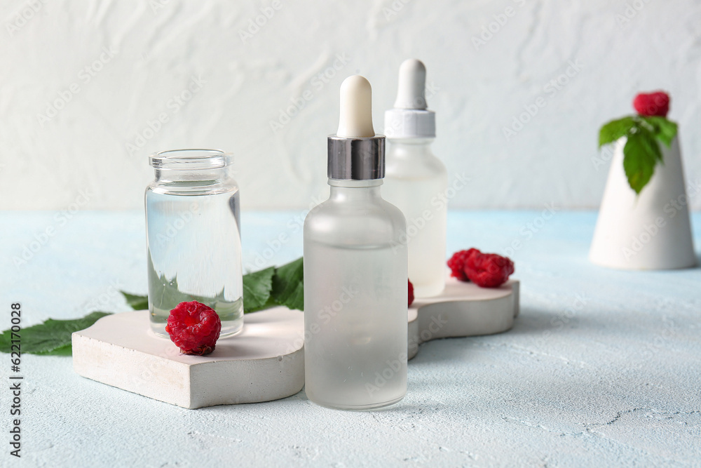 Decorative podium with bottles of cosmetic raspberry oil on blue table