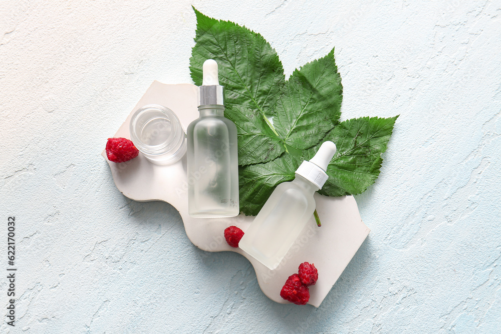 Decorative podium with bottles of cosmetic raspberry oil on blue table