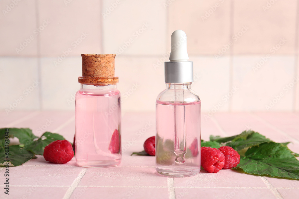 Bottles of cosmetic raspberry oil on pink tile background