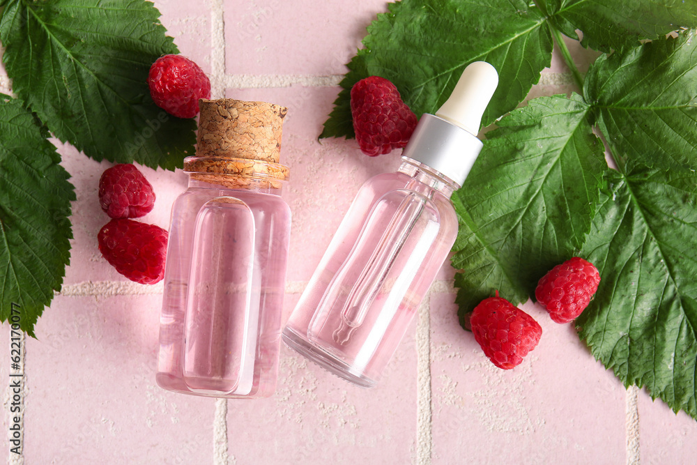 Bottles of cosmetic raspberry oil on pink tile background