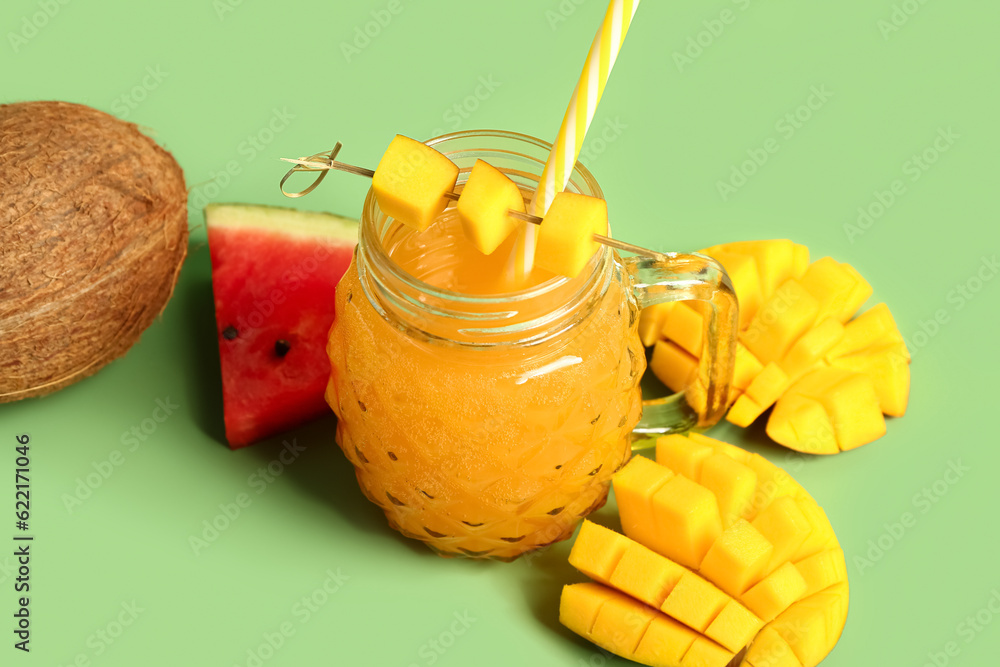 Mason jar of fresh mango juice with watermelon and coconut on green background