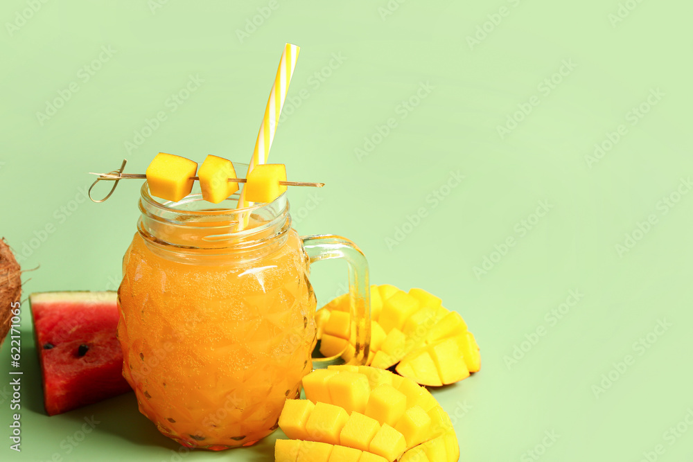 Mason jar of fresh mango juice with watermelon on green background