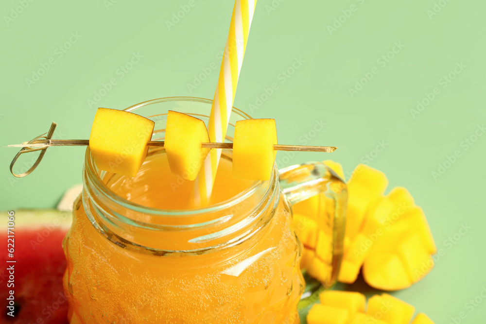 Mason jar of fresh mango juice with watermelon on green background