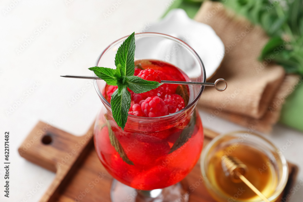 Glass of fresh raspberry lemonade and bowl with honey on white background