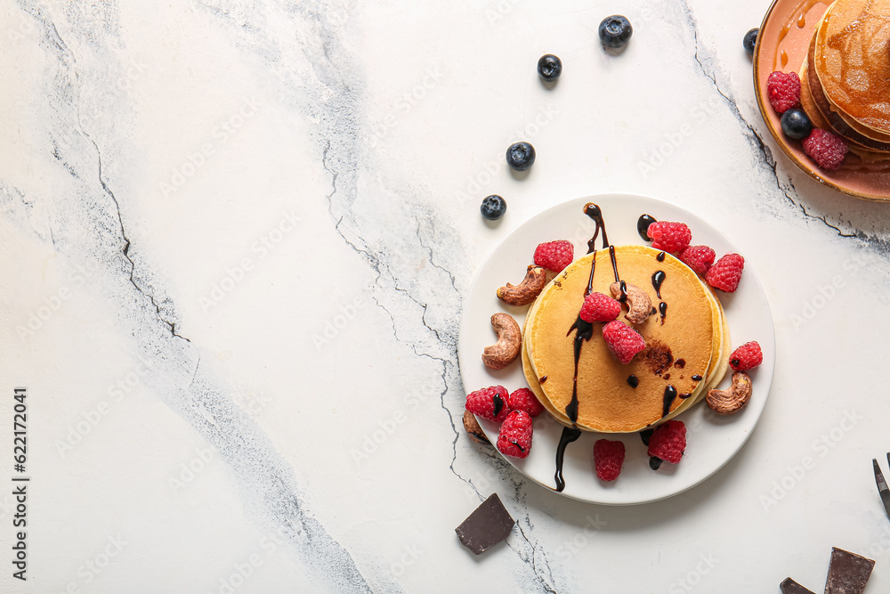 Plates of tasty pancakes with raspberries, nuts and blueberries on white marble background