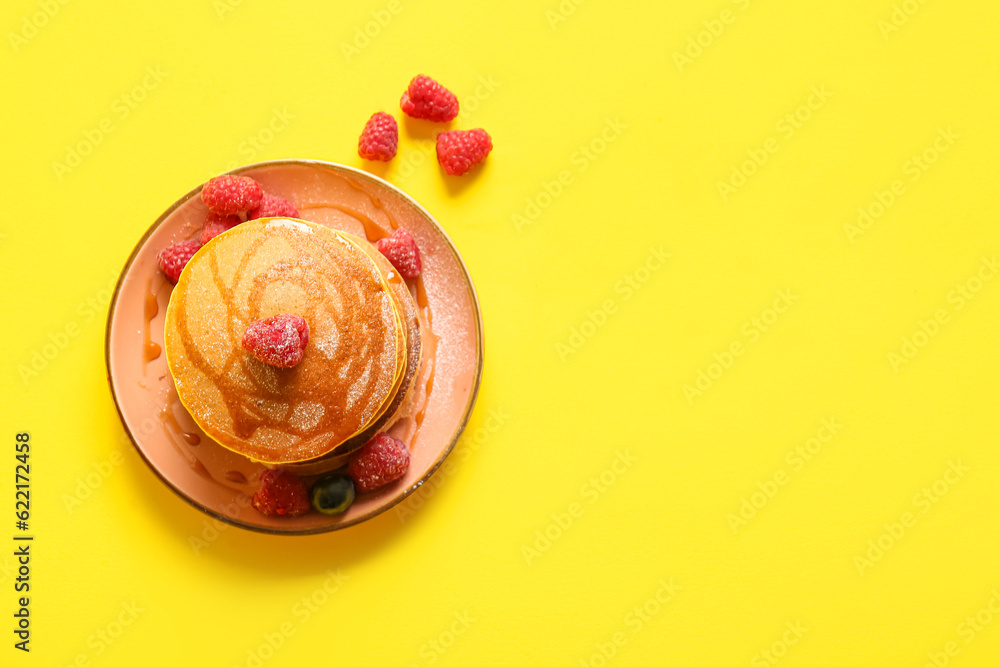 Plate of tasty pancakes with raspberries on yellow background