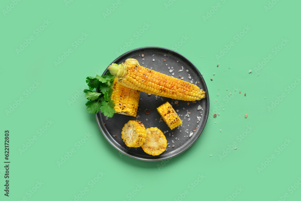 Plate with tasty grilled corn cobs and parsley on green background