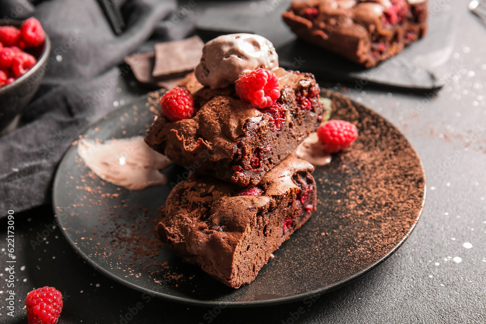 Plate with pieces of raspberry chocolate brownie and ice-cream on black background