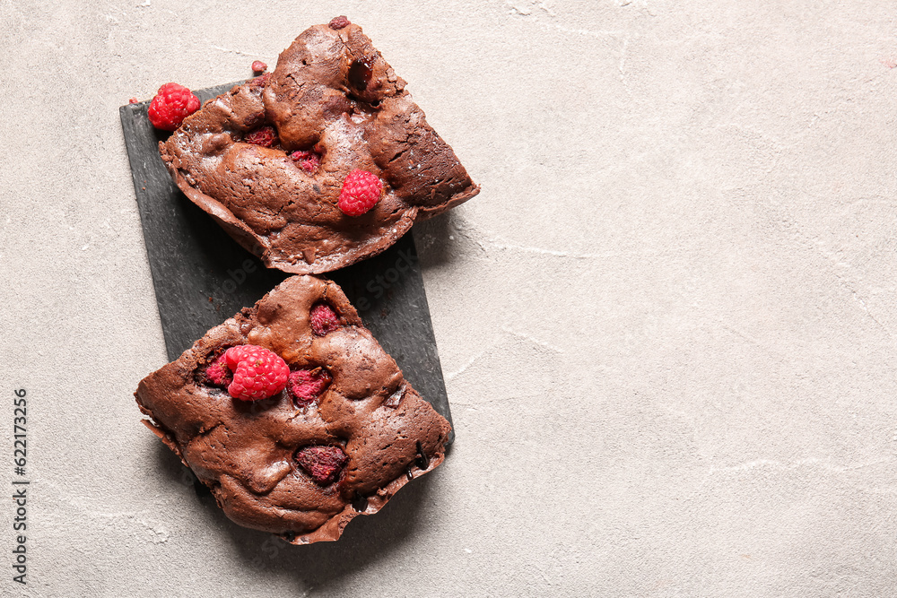 Board with pieces of raspberry chocolate brownie on grey table