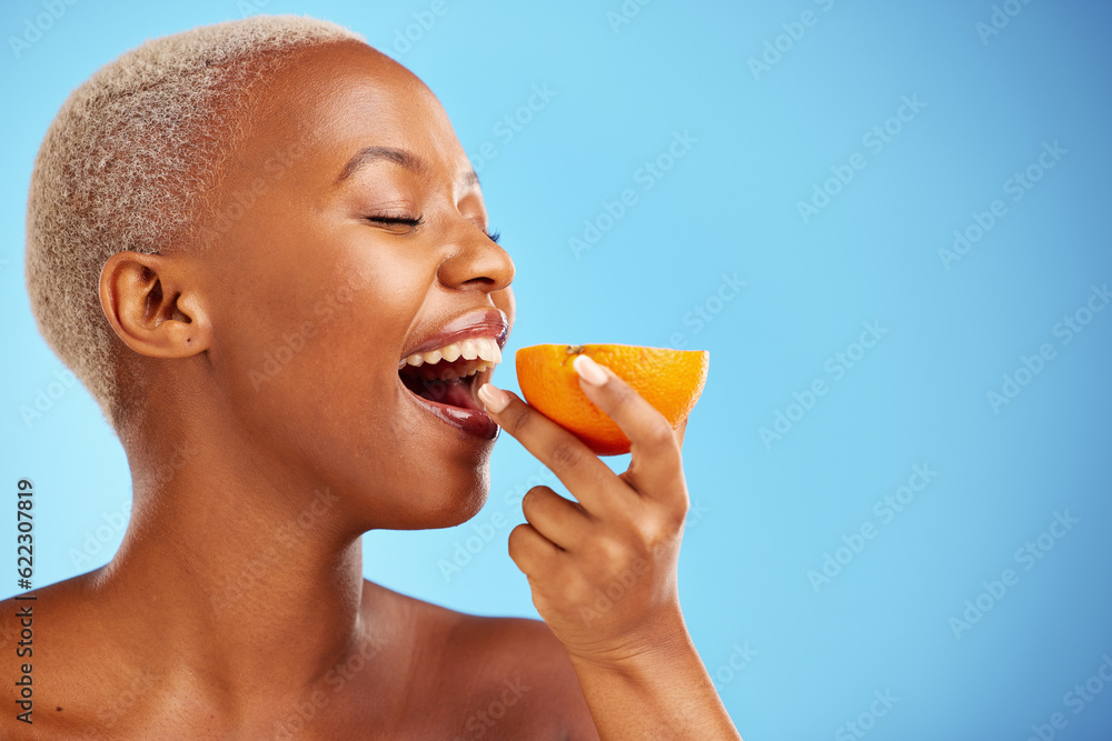 Orange, skincare and nutrition with a model black woman in studio on a blue background biting fruit.