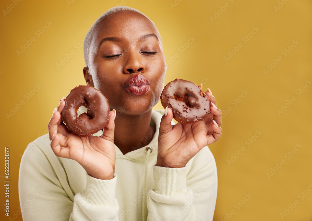 Face, kiss and donut with a black woman in studio on a golden background for candy or unhealthy eati