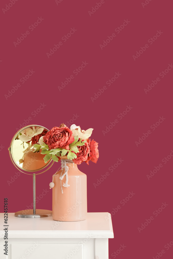 Vase with flowers and mirror on table near pink wall