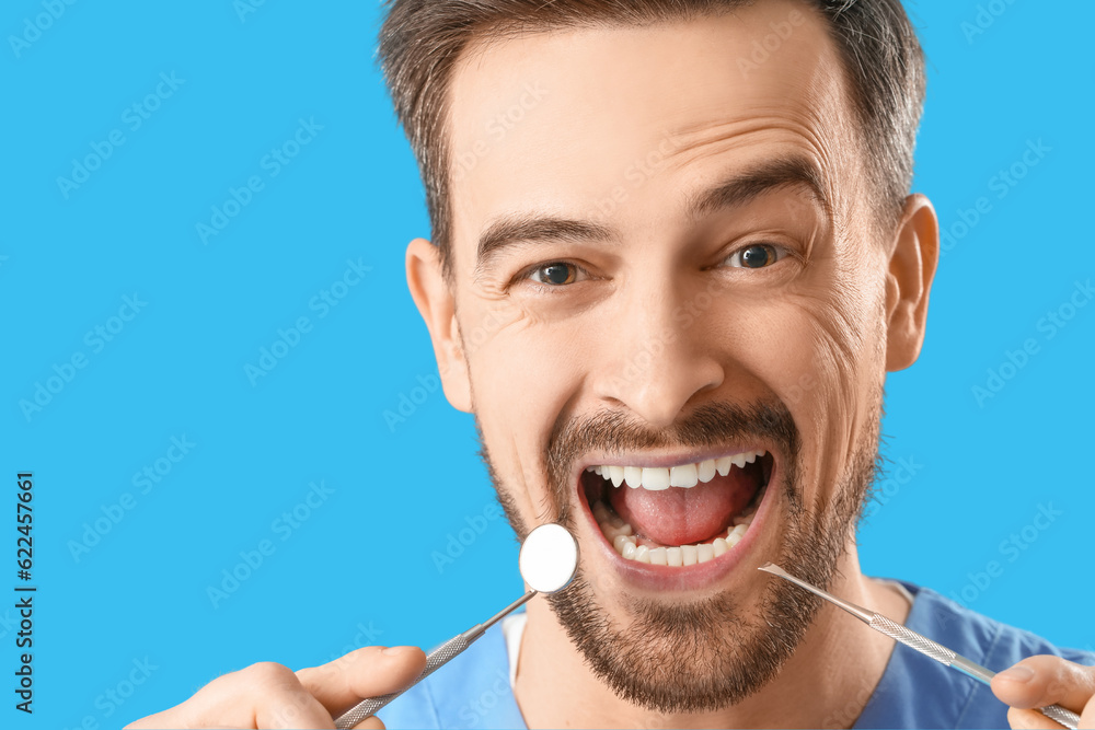 Happy male dentist with tools on blue background, closeup