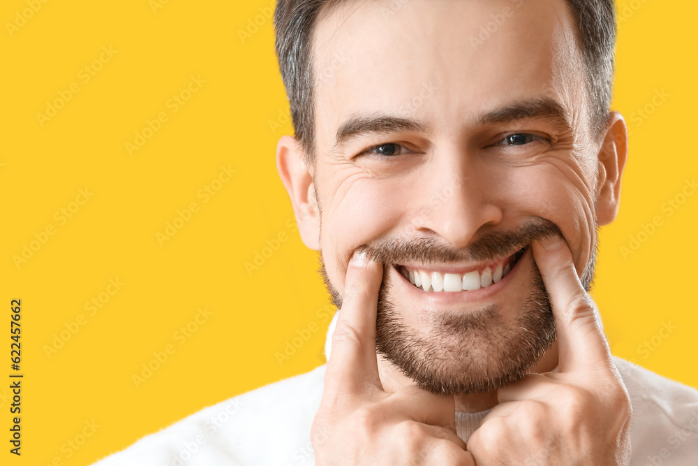 Smiling young man with healthy teeth on yellow background, closeup