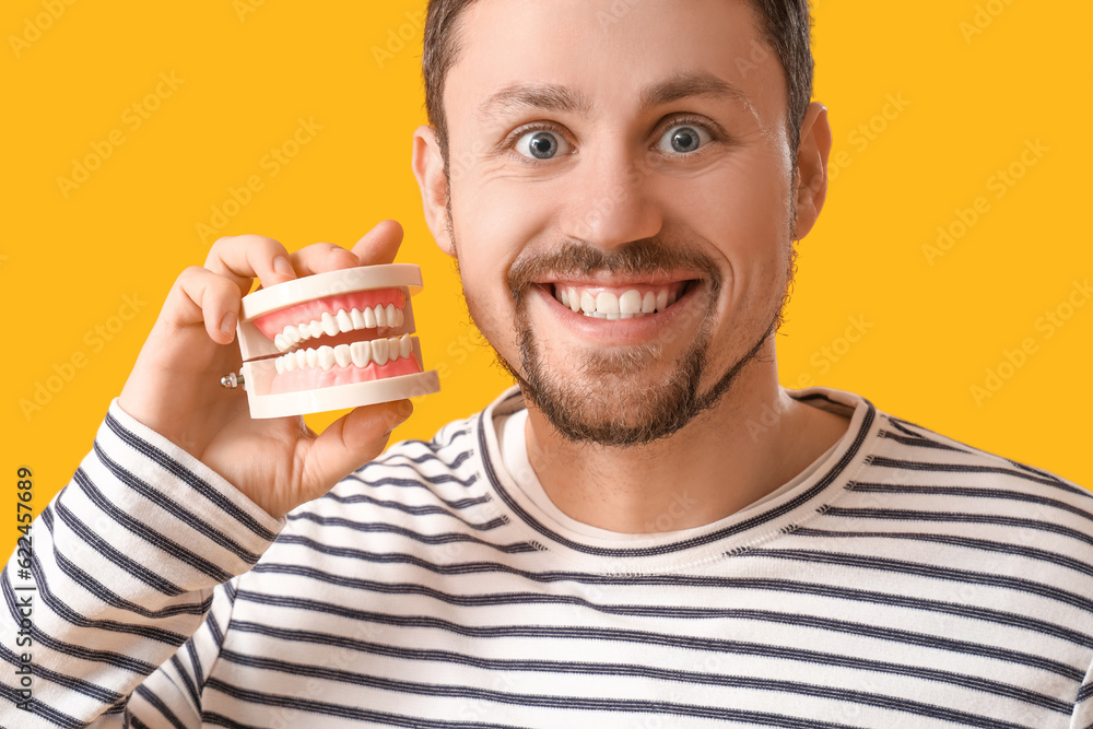 Young bearded man with jaw model smiling on yellow background, closeup