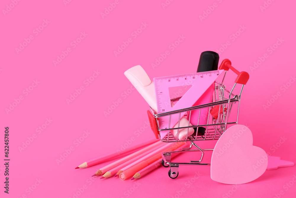 Shopping cart with different stationery on pink background