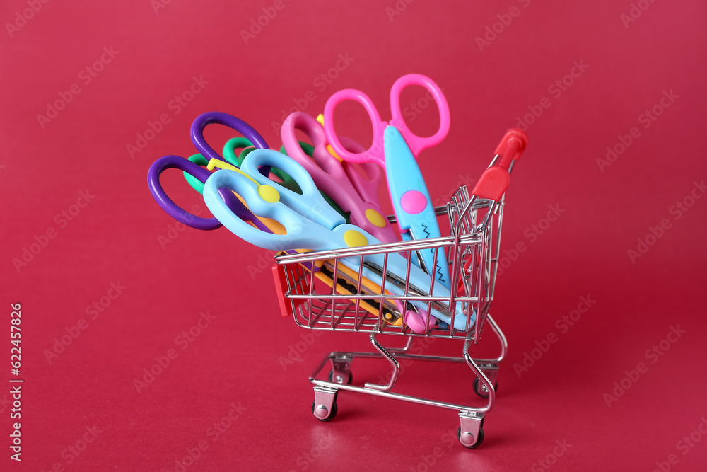 Shopping cart with different scissors on color background