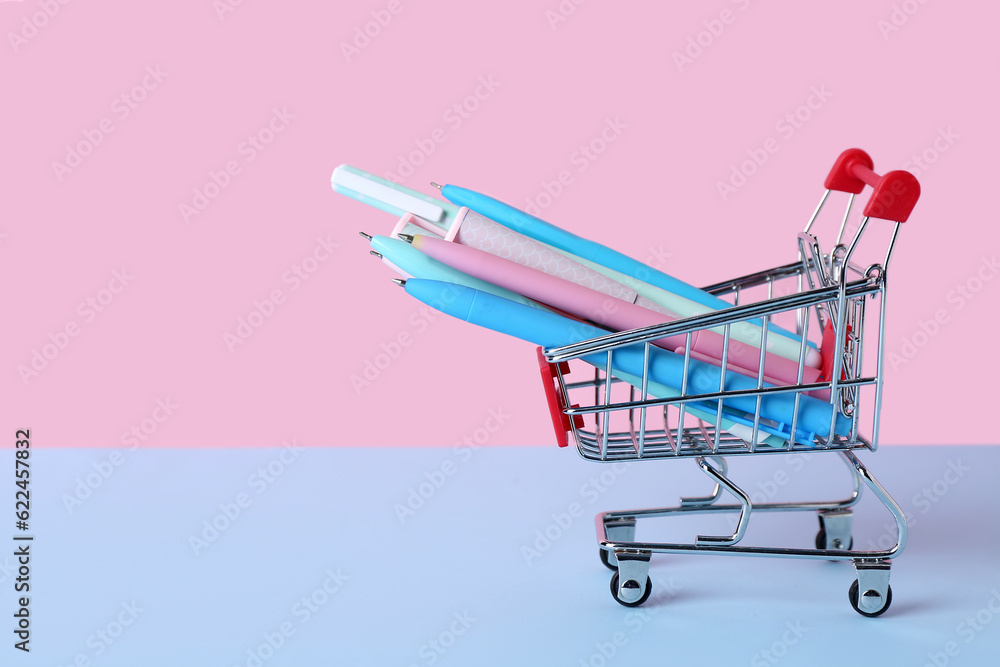 Shopping cart with different pens on color background