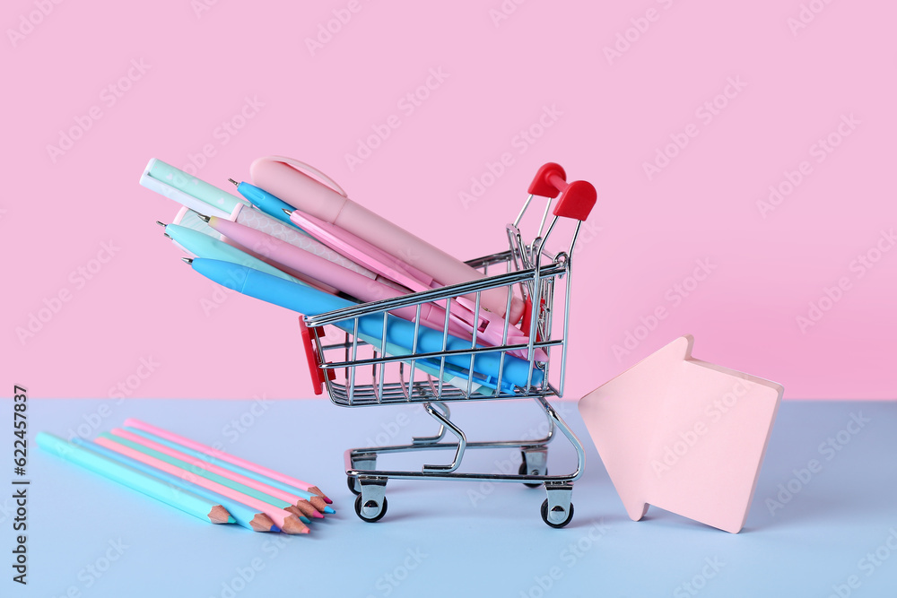 Shopping cart with different pens, pencils and sticky notes on color background