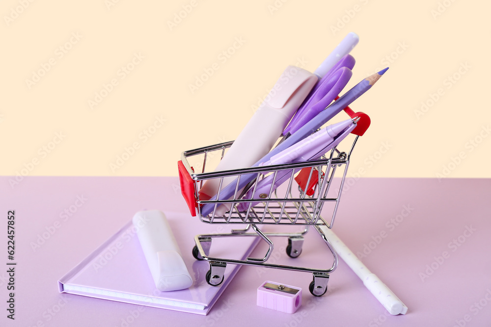 Shopping cart with stationery on color background