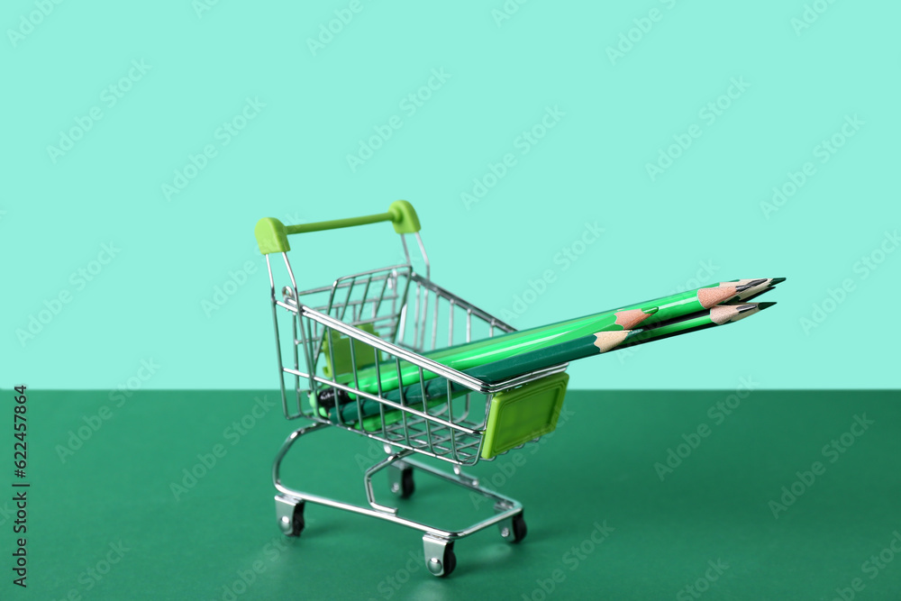 Shopping cart with pencils on color background