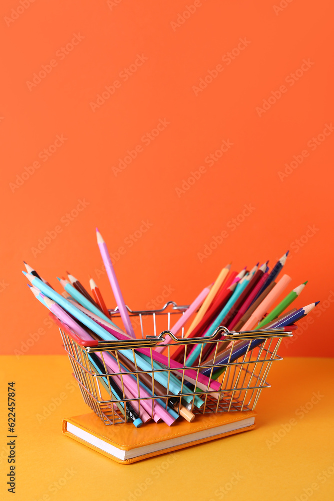 Shopping basket with pencils and notebook on color background